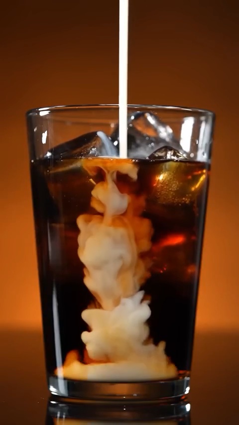 Milk swirling into a glass of Cool Drip cold brew over ice